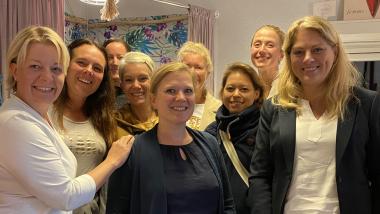 Neun Frauen stehen in einer Boutique und lachen.